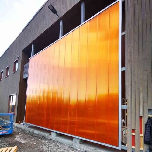 Oranssin värinen polykarbonaattijulkisivu asennuksessa